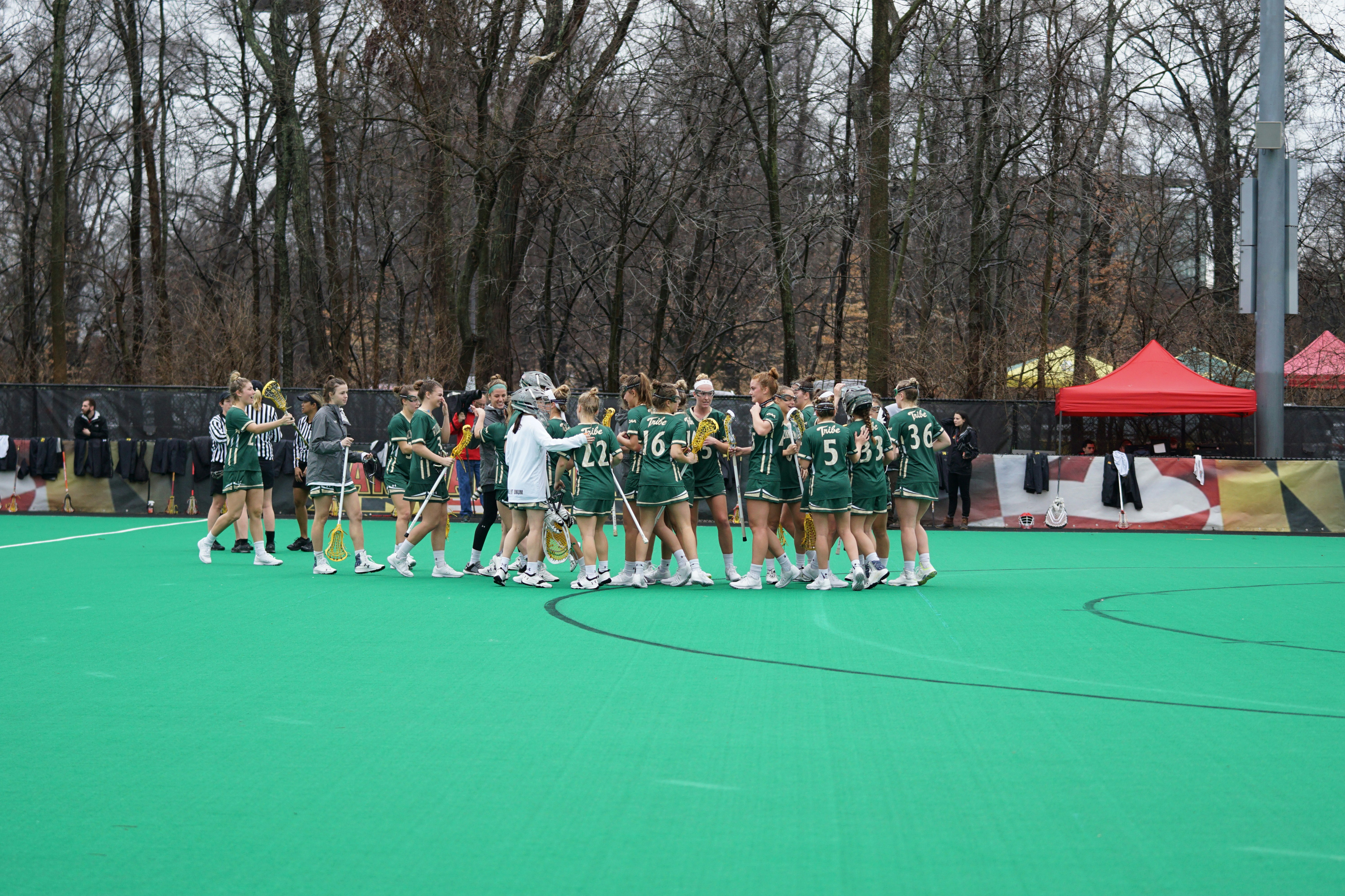 A group of women's lacrosse players gather on the field.